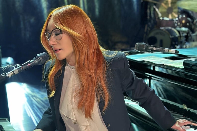 A woman with eyes closed is playing 2 keyboards and singing into a mic.