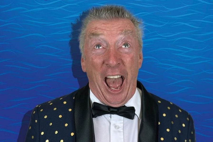 A man is appearing to shout with eyes looking upwards, wearing black jacket with small gold dots and black bow tie against blue wavy background.