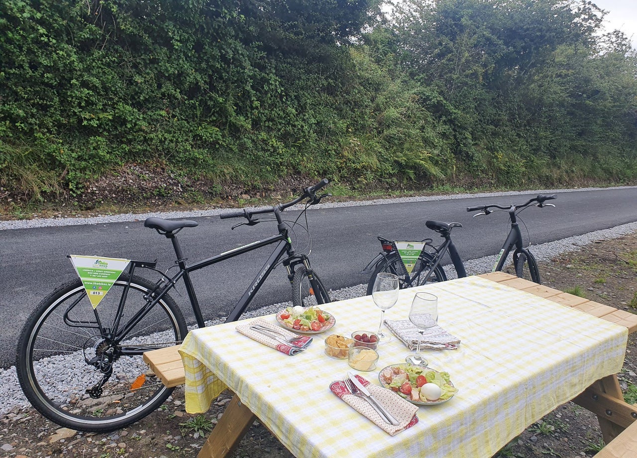 Two bikes parked by a picnic table with food and wine glasses