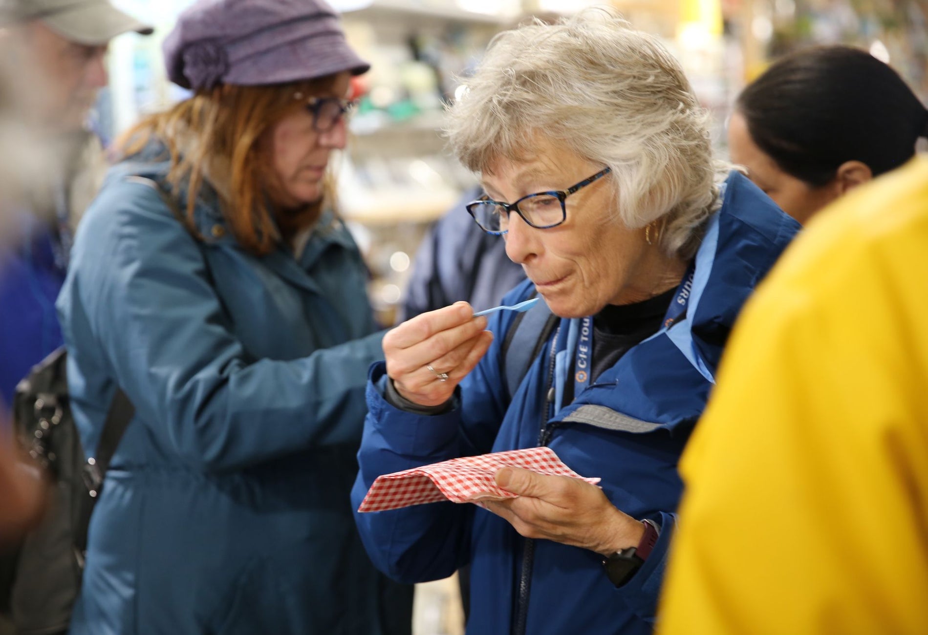 Person holding a small plastic spoon sampling food from a red and white napkin