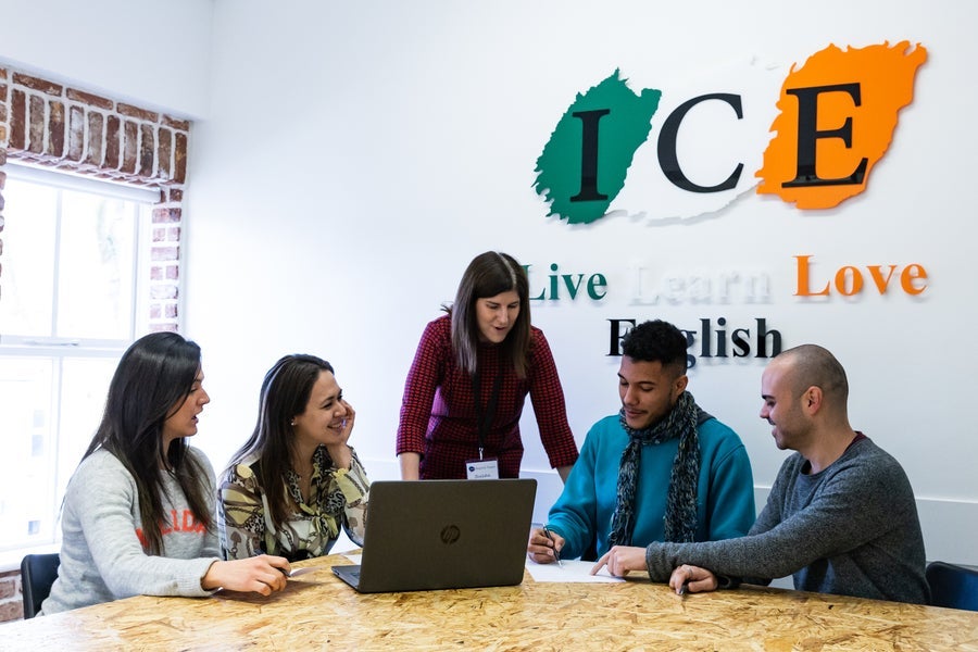 Four students and a teacher in a study group beneath the logo of the language school