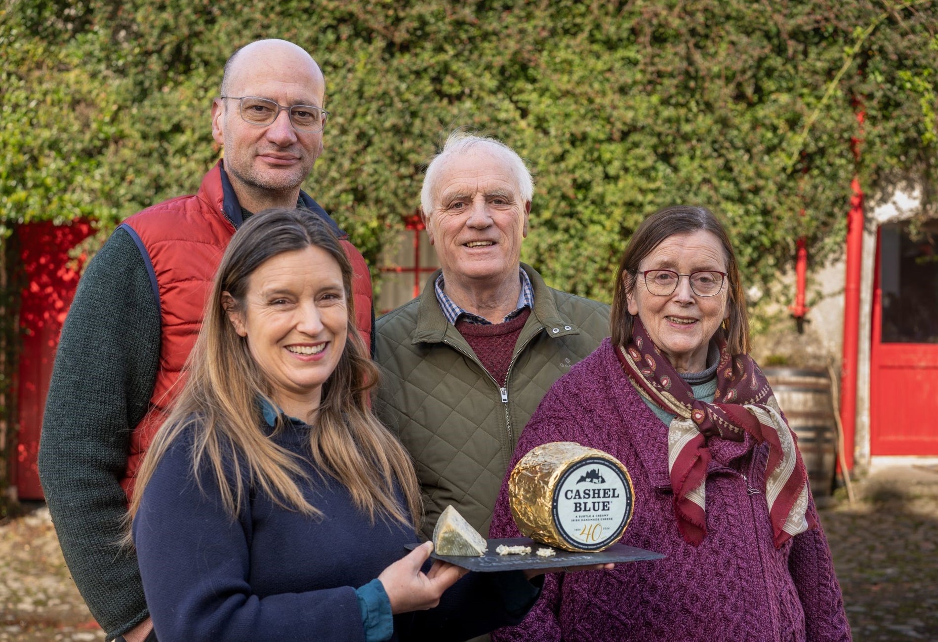 Four people smiling with one person holding a slate with cheese on it