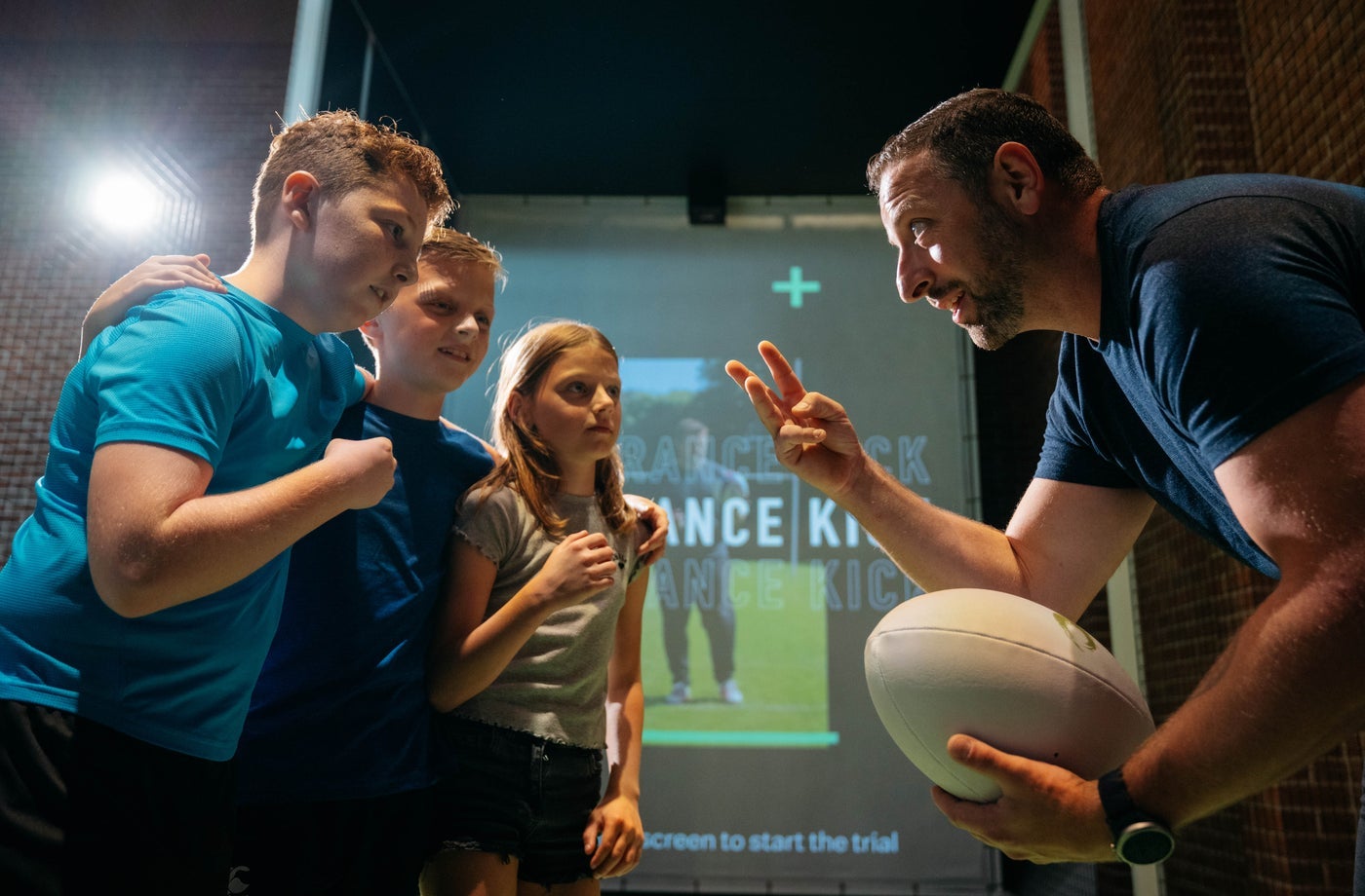 Three children with a staff member holding a rugby ball