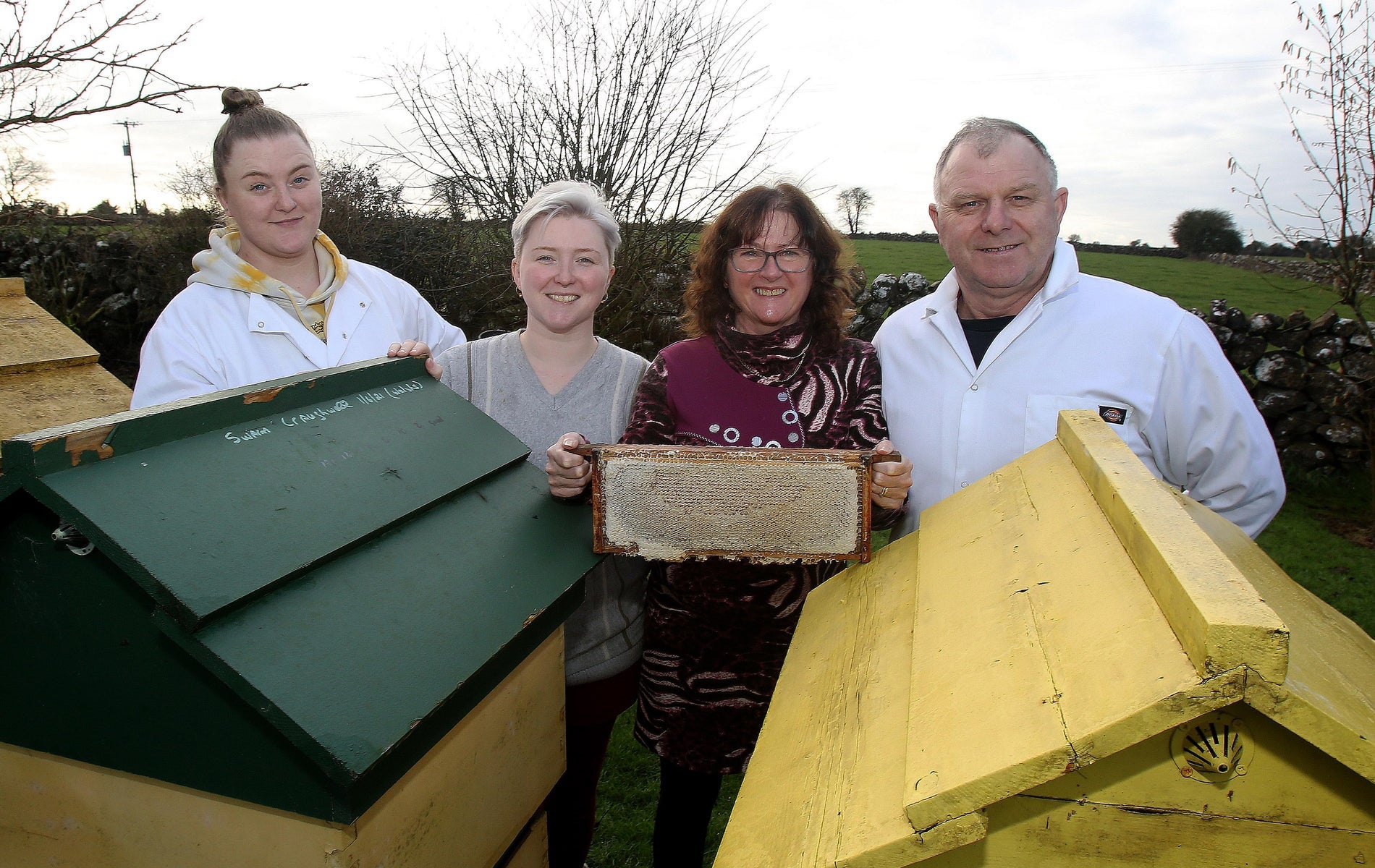 Four people posing for the camera in front of bee hives
