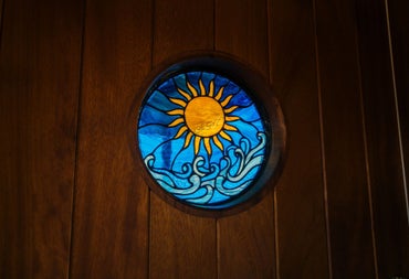 Round stained glass window with sun and wave design set into a wooden sauna wall