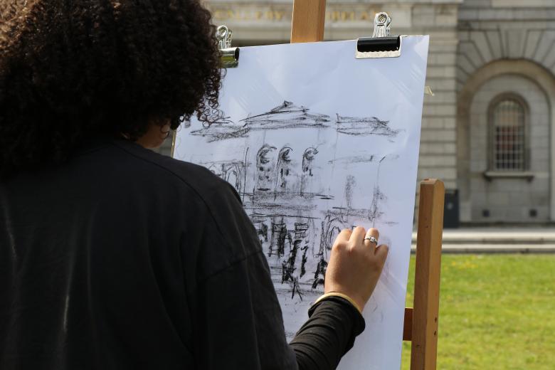 Rear view of person drawing on easel outdoors in front of a building