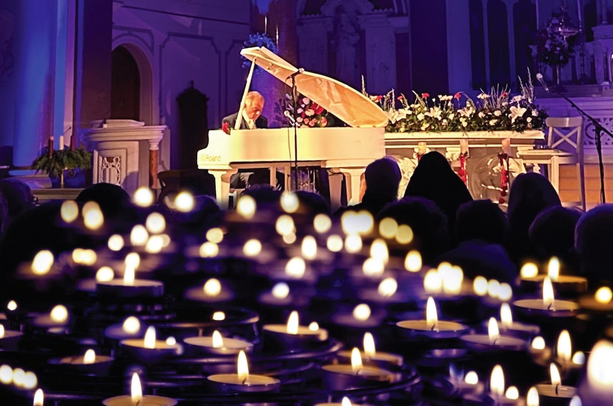 In the distance a man playing a white grand piano with lots of blurry candles in the foreground.