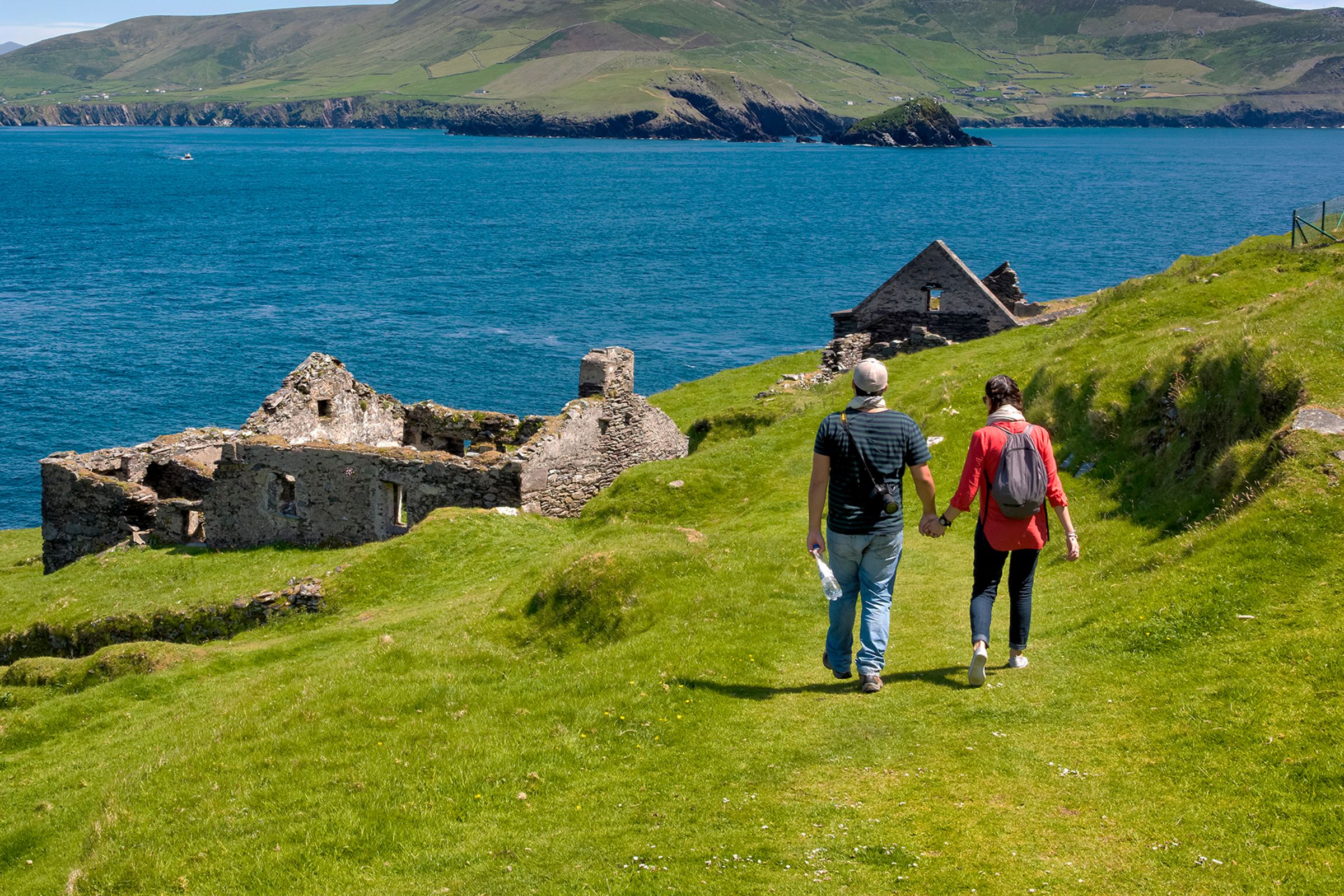 Two hikers walking on a grassy trail near abandoned buildings on Blasket Islands, Kerry.