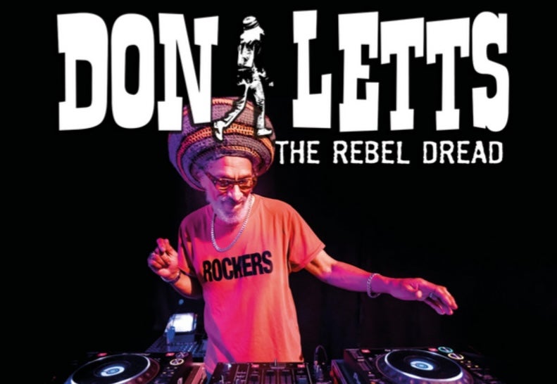 A man in T-shirt and large hat is standing behind a record mixing deck