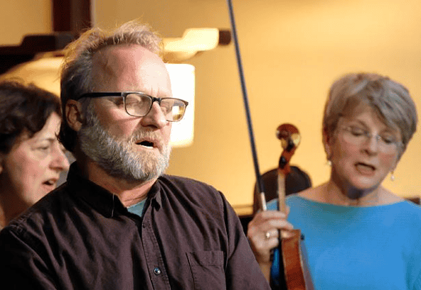 A seated man is singing with his eyes closed