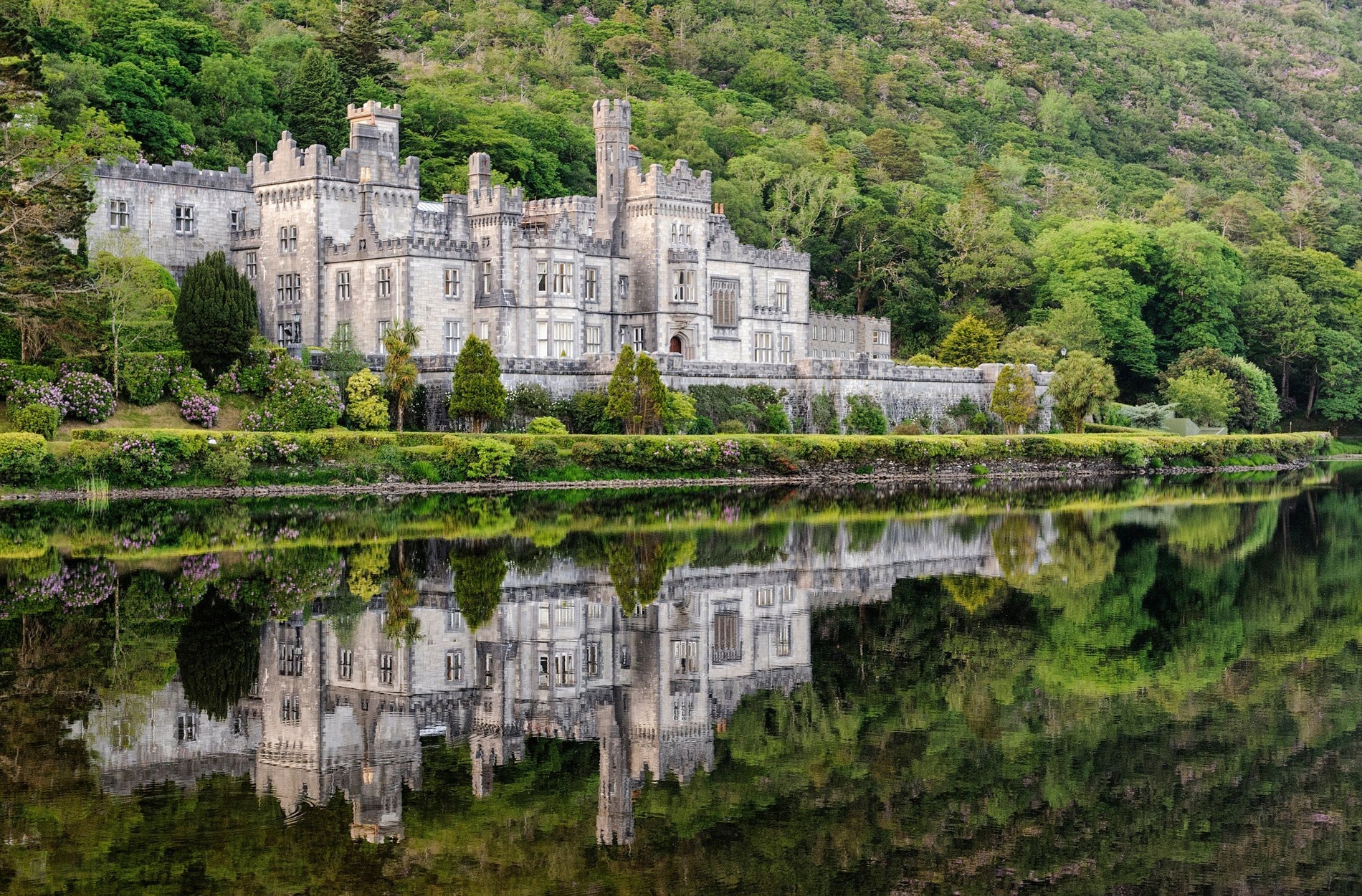 Kylemore Abbey reflected on the surface of a lake with a mountain of shrubs and trees behind it