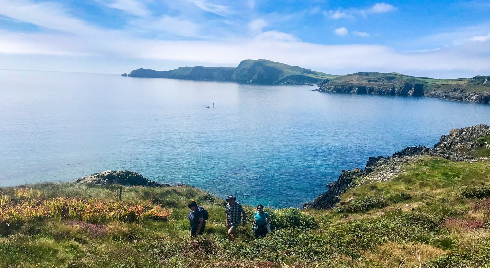Three people on a walking trail with a view of the West Cork coastline in the background
