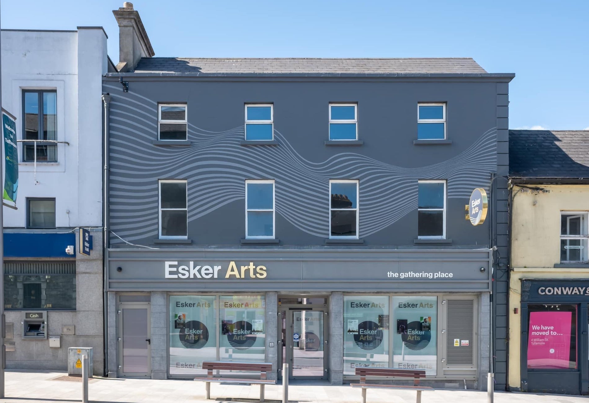 Grey exterior of a building on a street with two benches in front