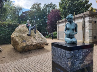 The playful reclining statue of Oscar Wilde perched on a boulder in Merrion Square, alongside one of the sculpture's companion figures — a popular photo stop on Dublin's literary trail.