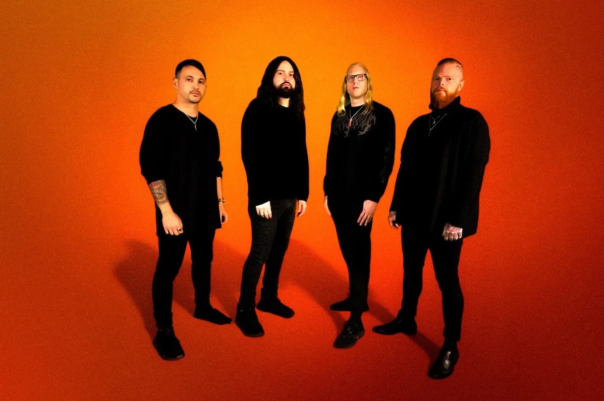 Illinois progressive metal band Born of Osiris, 4 serious looking men dressed all in black, against plain orange background.