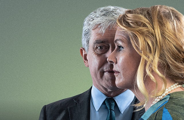 A man in a suit looking ahead with a woman in side profile slightly in front of him.
