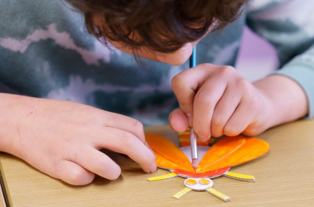 Children's art workshop with Cas McCarthy, a child leaning over a small piece of art work, painting.