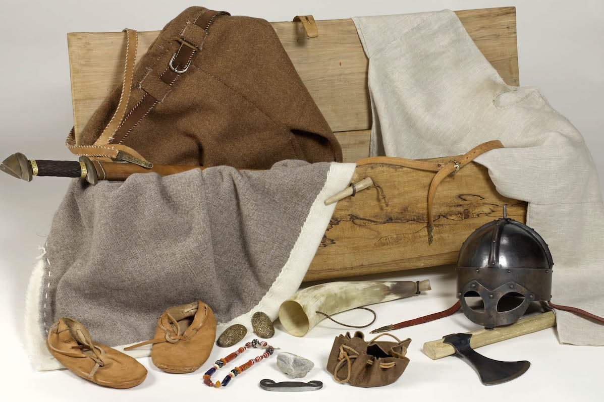 A replica Viking Chest with handmade clothes, booties and helmut with items of jewellery and axes.