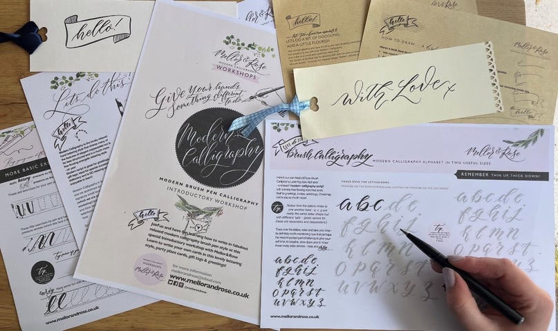 The Joy of Calligraphy - various sheets of paper containing text and letters with a hand holding a pen.