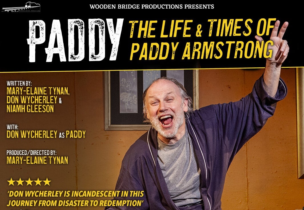 A man in a dressing gown is shouting with arms outstretched on a stage set