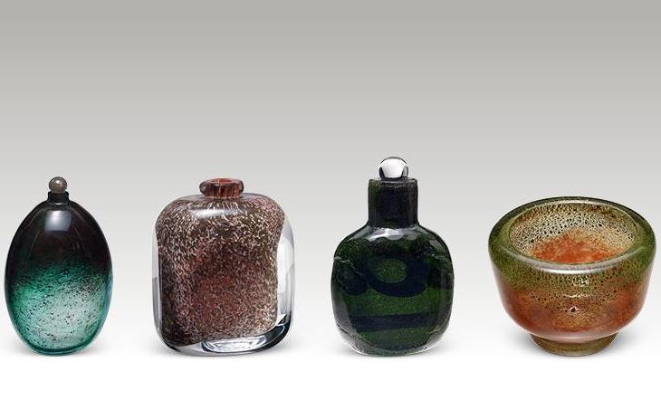 A row of 4 small different coloured glass vases against plain light grey background.