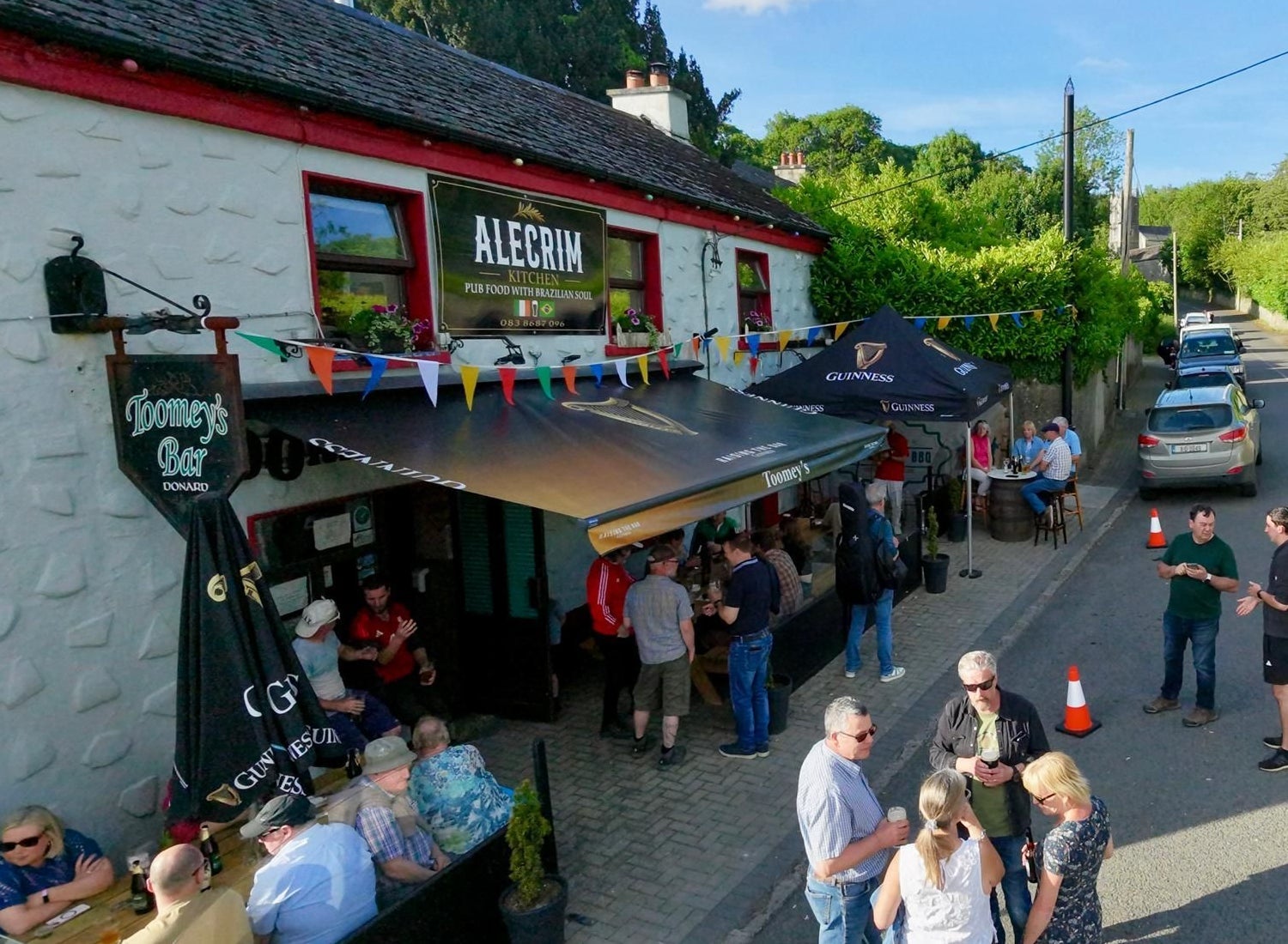 People gathered outside Alecrim Kitchen and Toomey's Bar with outdoor seating and colourful bunting