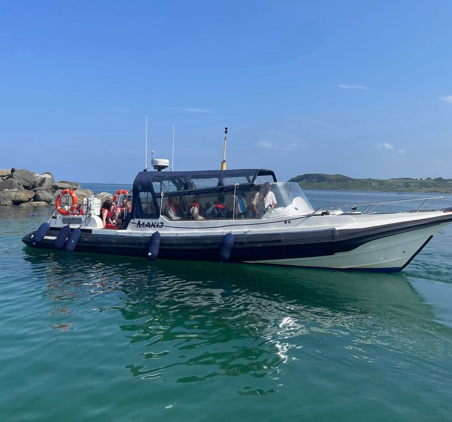 A passenger boat cruising on calm blue water with rocky shoreline and green hills in the background