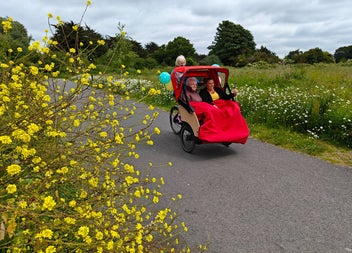 Two people sitting in a trishaw with someone peddling a bike behind them
