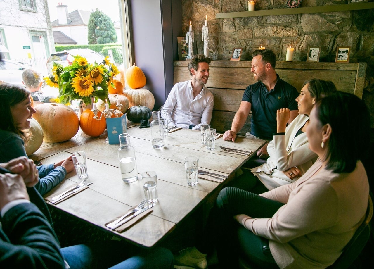 A group of people sitting at a table with pumpkins and sunflowers on the window