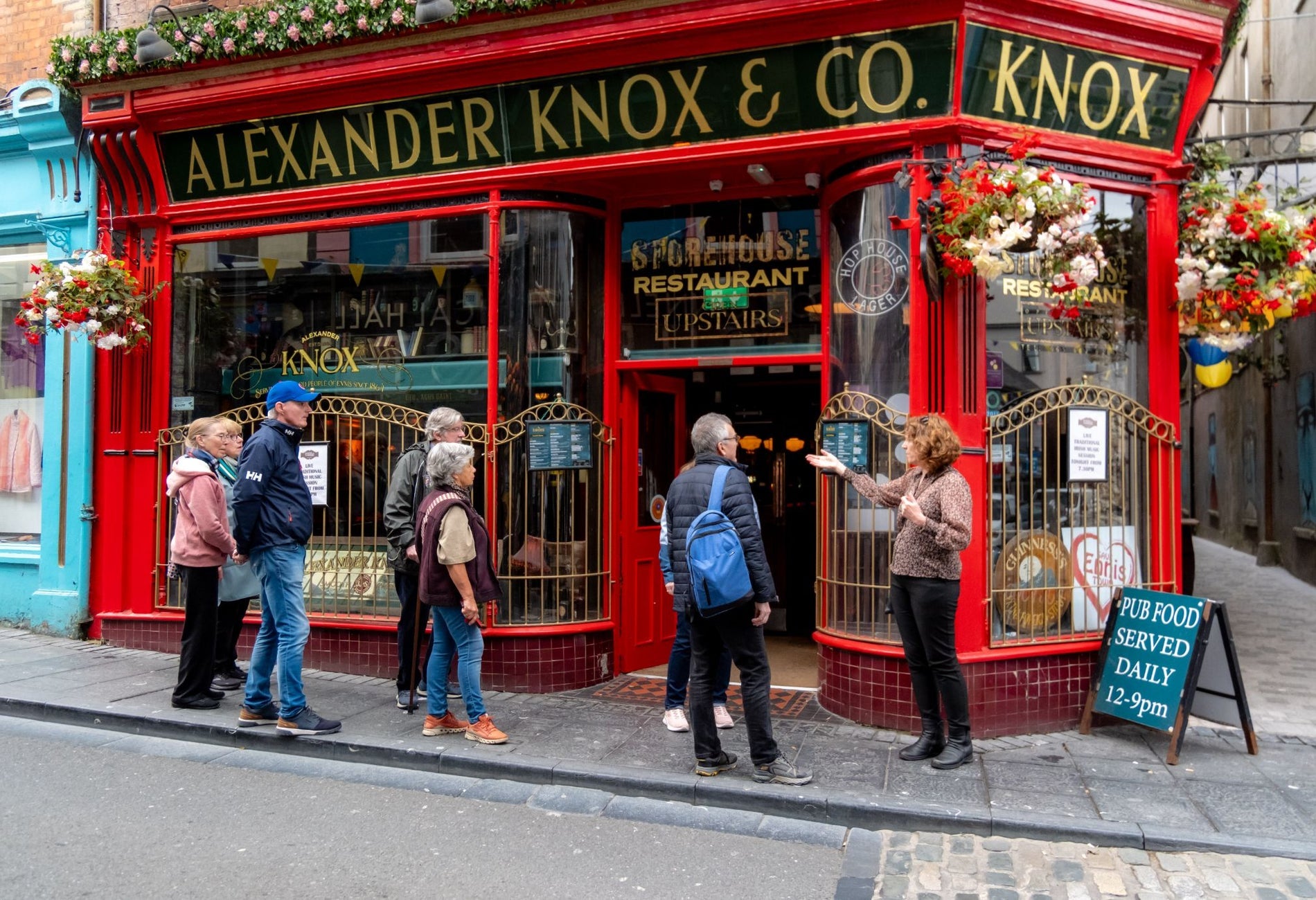 A group of people gather outside a bright red pub on a narrow city street