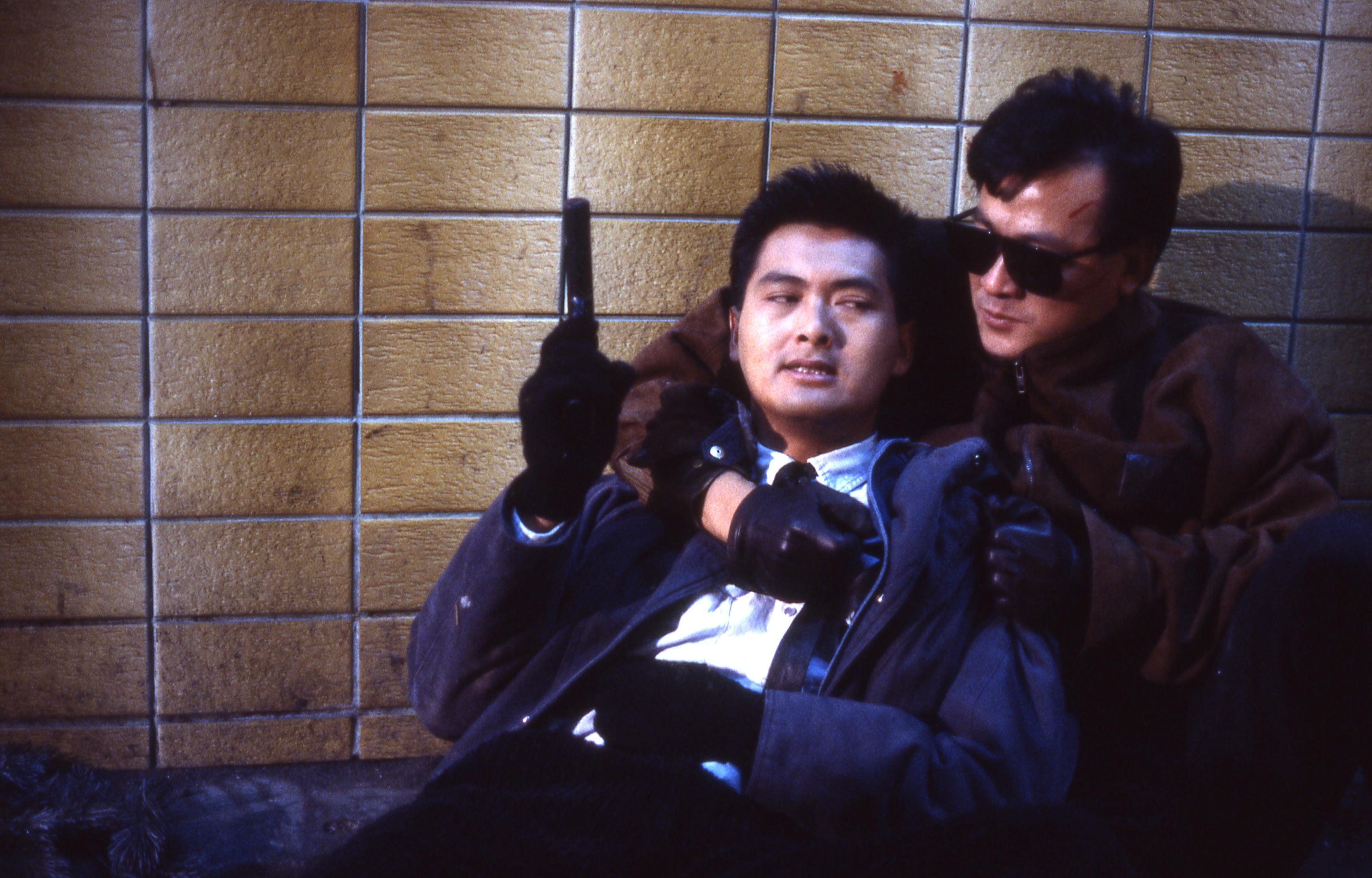 A man with a pistol is on the ground, being held from behind by another man.