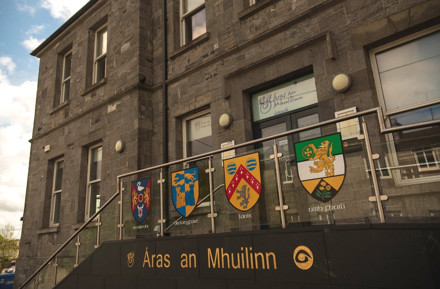 A large building with steps and metal hand rail lined with family crests leading to a door