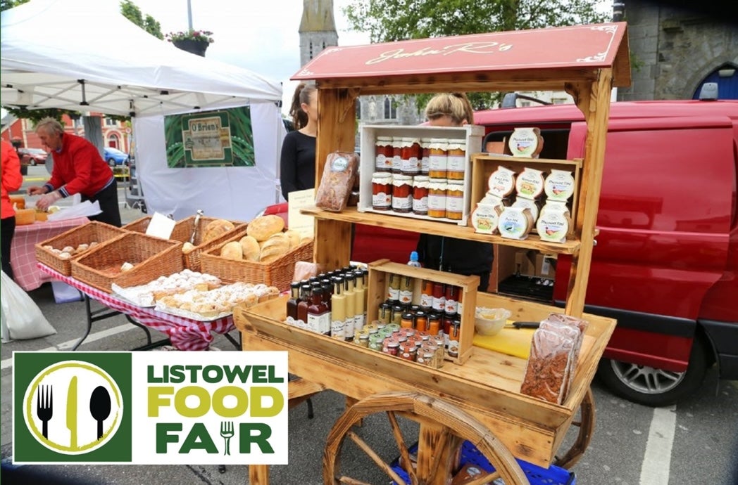 Listowel Food Fair 2025 - A wooden cart holding displays of various potted sauces beside table with wicker baskets containing different baked goods and loaves of bread.
