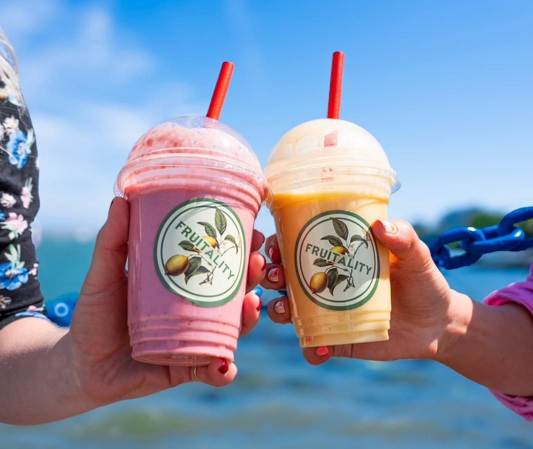 A close up of two people holding plastic cups with straws and colourful liquids