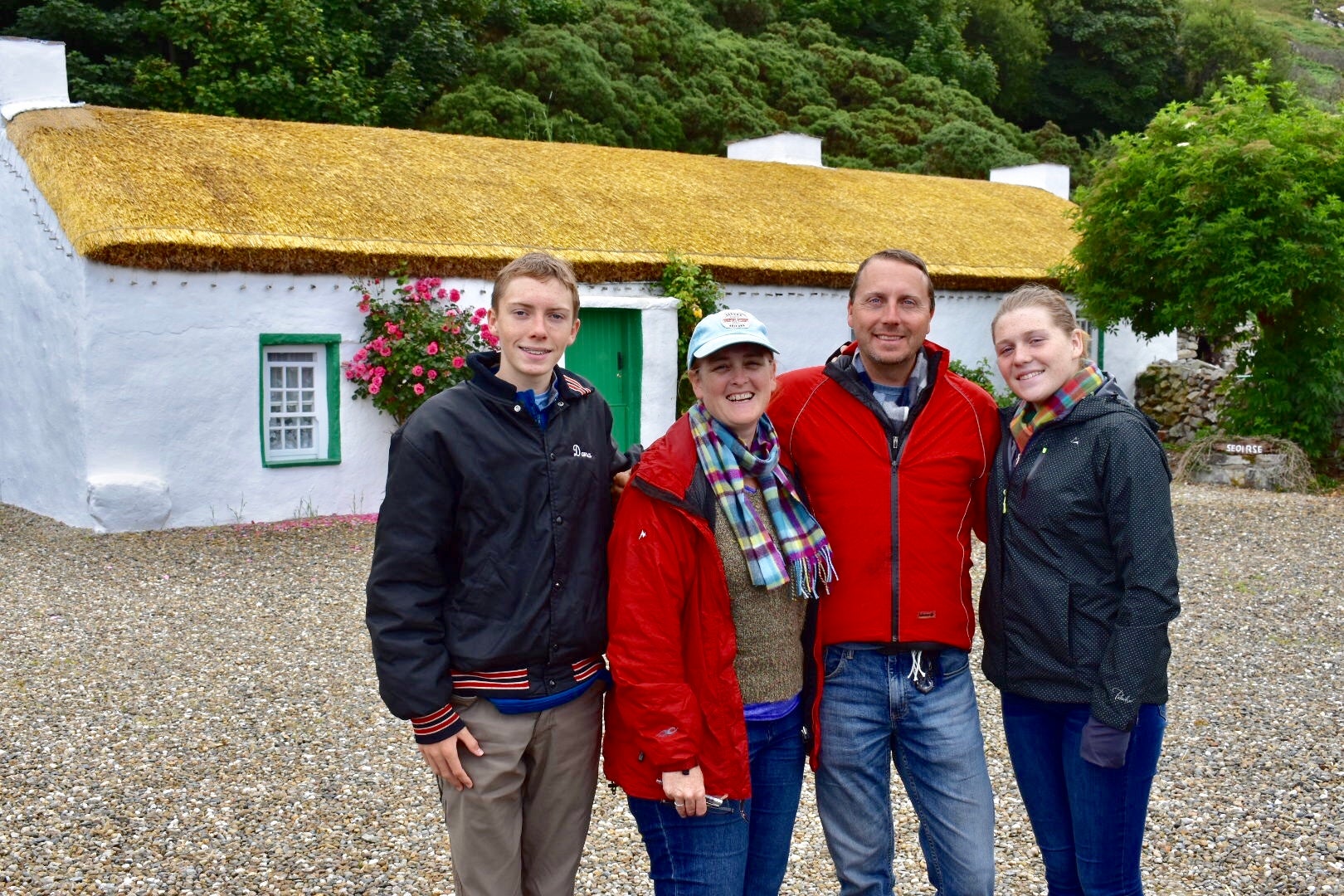 A family of four standing in front of a thatched cottage for a group photo
