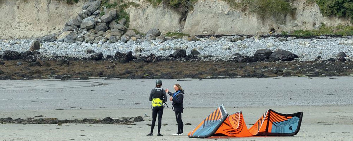 Two people on beach with orange and blue kite
