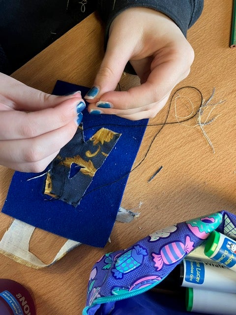 Someone is a creating an artwork by sewing a piece of fabric onto something.