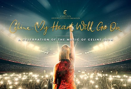 Rear view of woman in red dress with right arm straight up in the air looking out over an audience