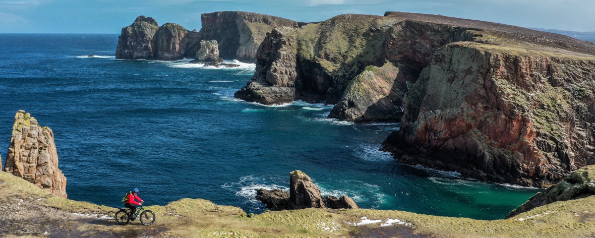 A cyclist rides past cliffs and sea views