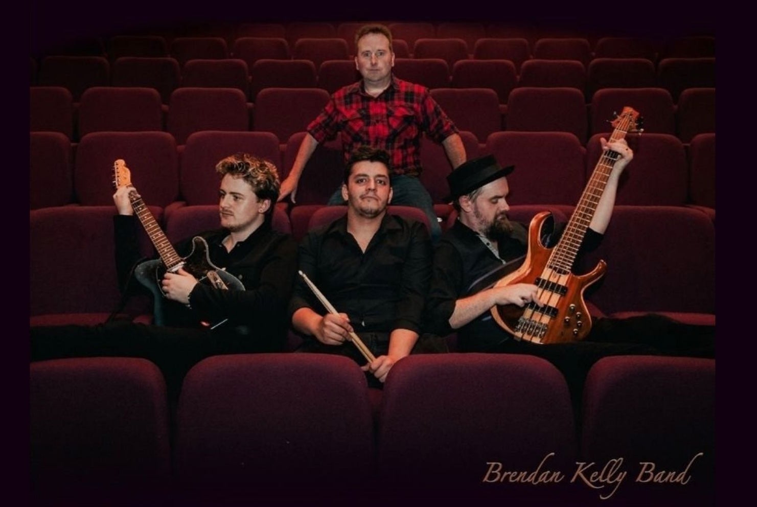 A group of 4 men with musical instruments seated in empty theatre seats