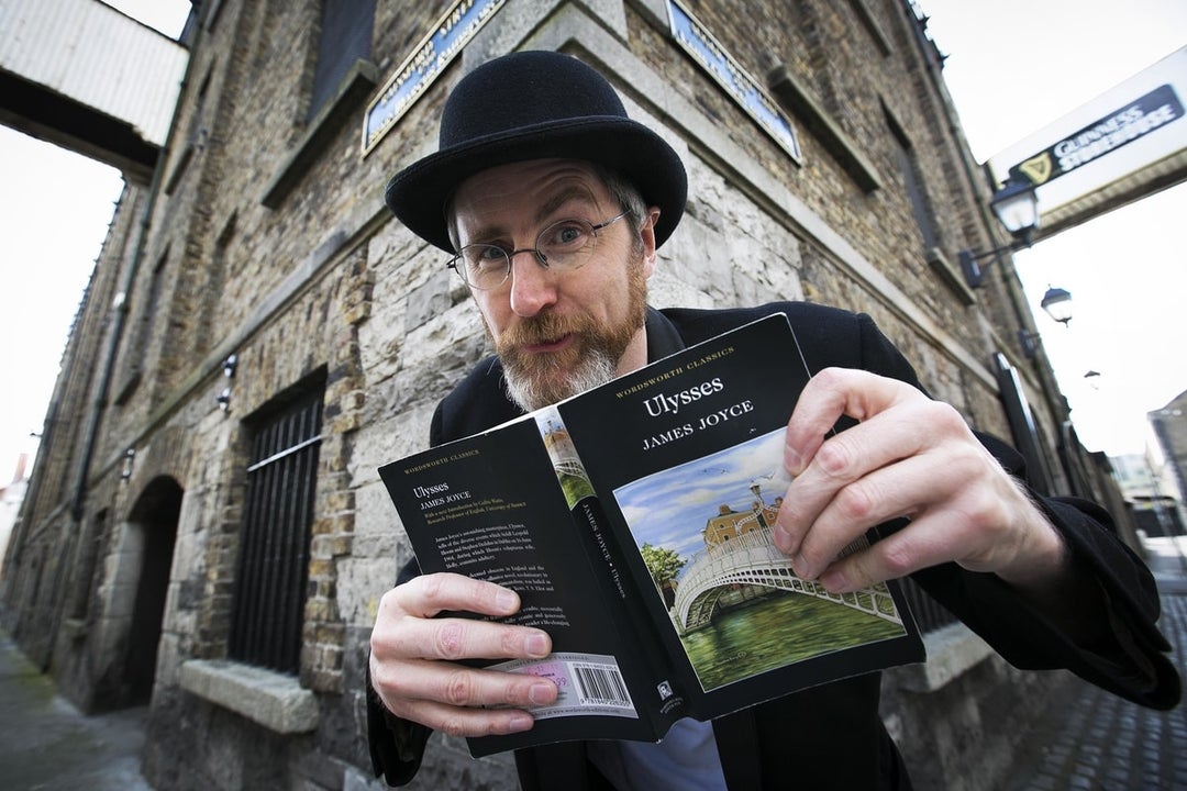 A man in black suit and hat is holding open a book in front of a corner building