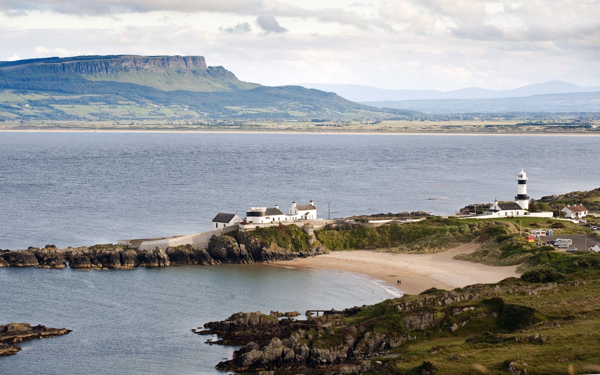 A horse shoe shaped beach with a lighthouse overlooking it