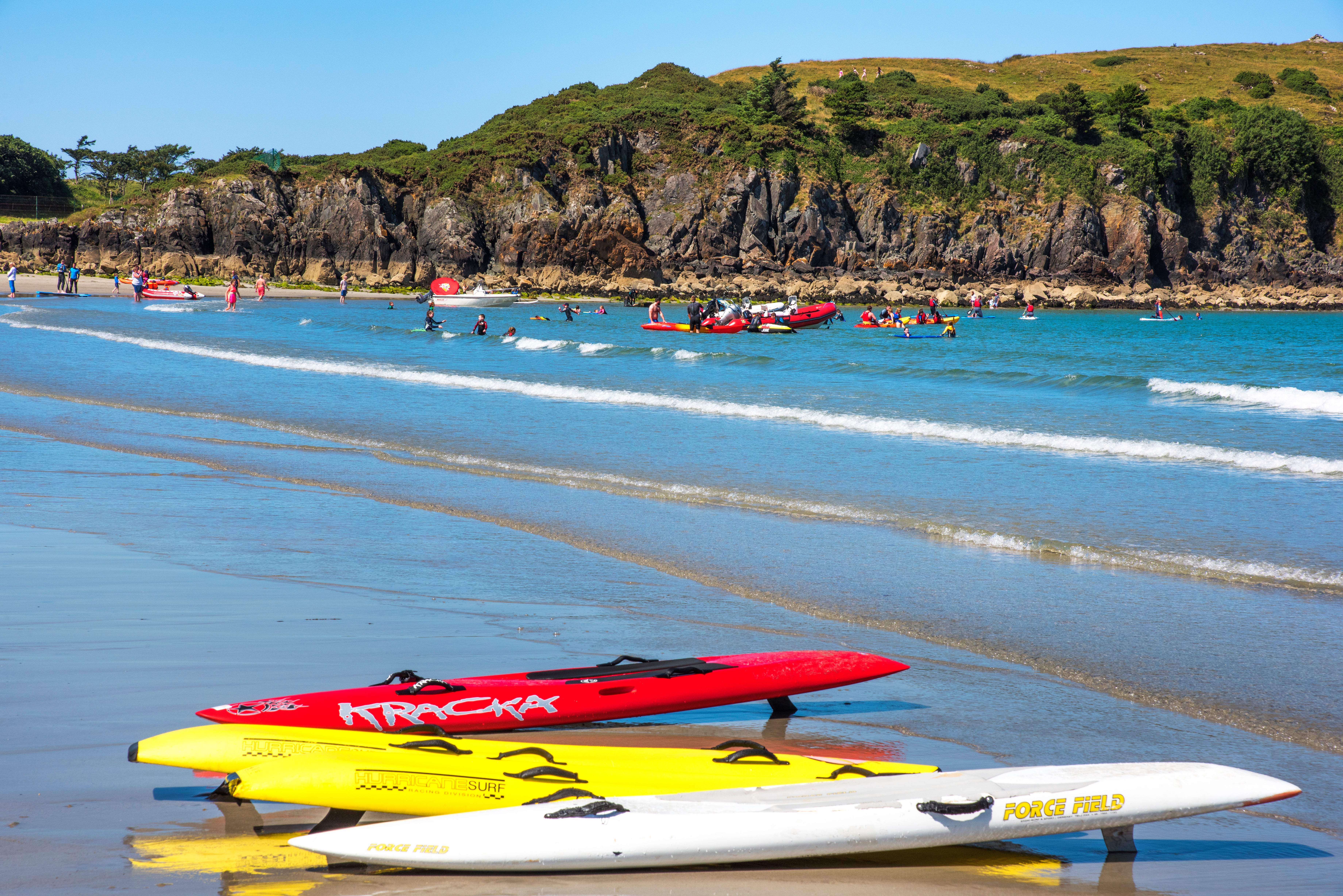 Surfboards lying on the shore with people playing in the sea against a backdrop of mountains at Marble Hill Beach, Donegal