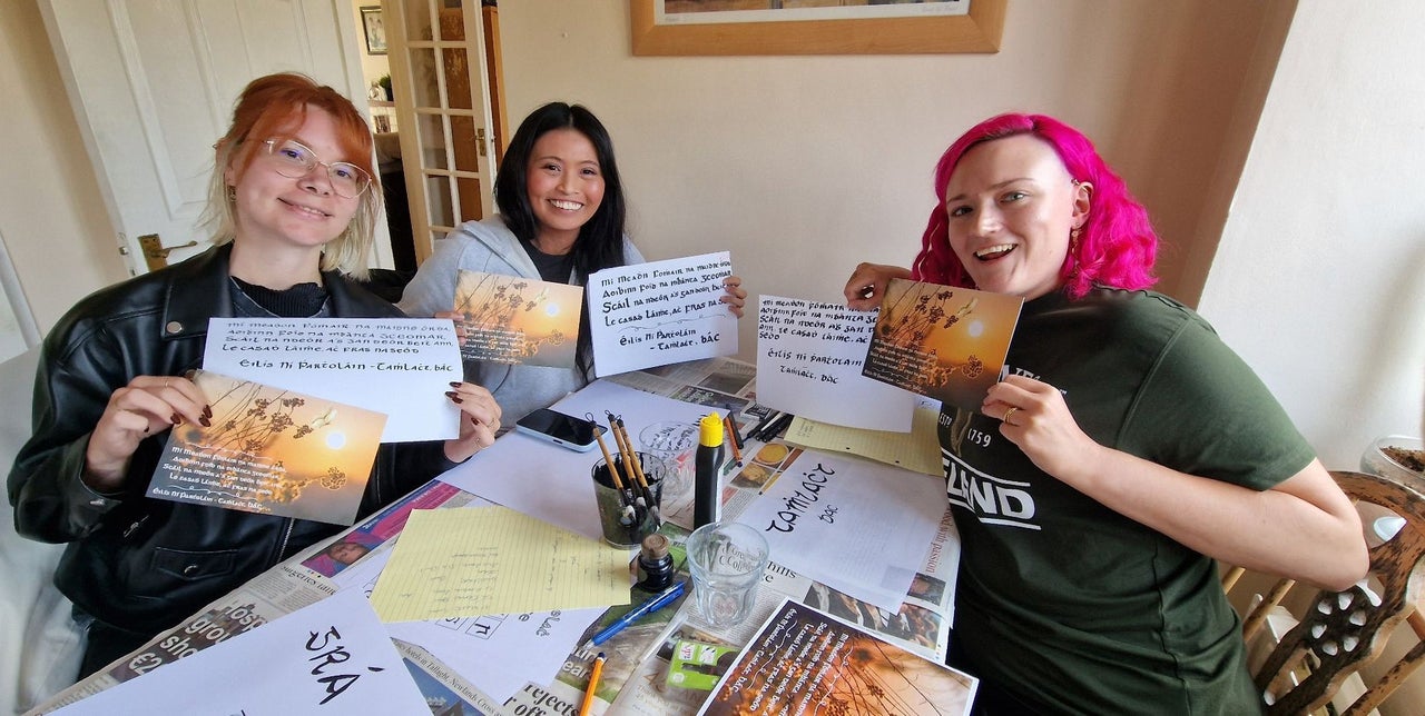 Three girls holding up cards with Irish calligraphy on them
