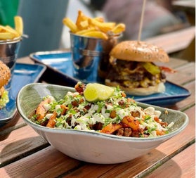 Burger and dressed fries meal with drinks on a table at an outdoor dining area