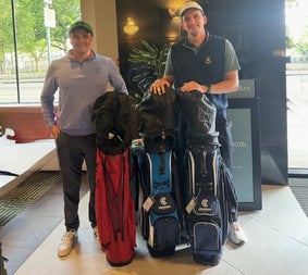 Two people with three golf club bags standing in a hotel lobby
