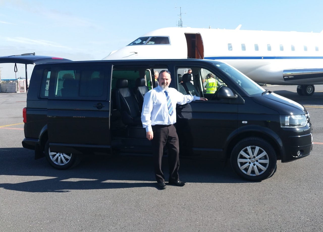 A driver standing at his van with an airplane in the background