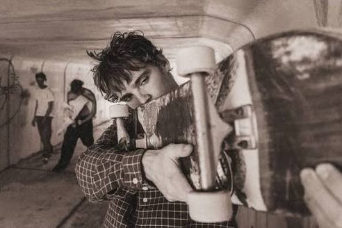 A close up of man holding up a skateboard horizontally to his shoulder.