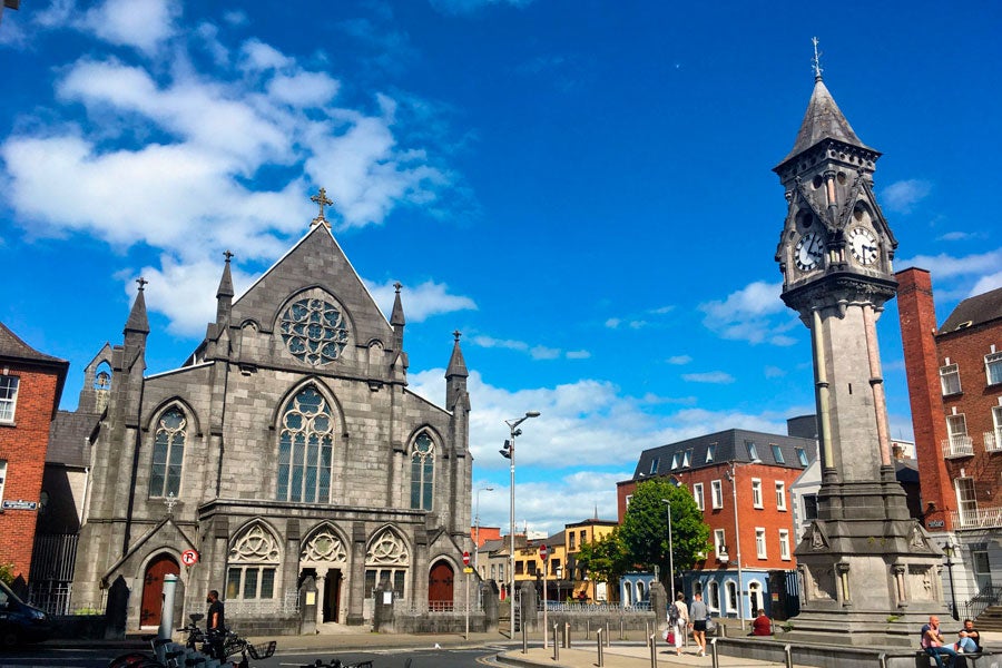 Tait's Clock in Limerick City with a church in the background against a blue sky