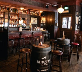 Traditional pub interior with a wooden bar high stools and barrel tables in a warmly lit setting